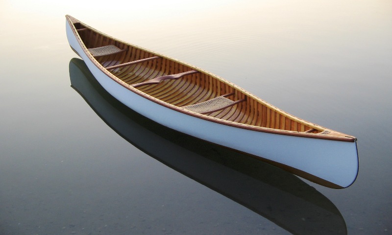 Algonquin Canoe rests in the water - White Canvas and Shellac finnish